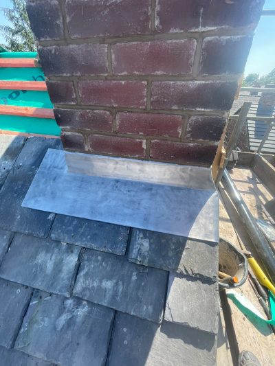 New lead apron and soakers dressed around the base of a chimney on a Stockport slate roof