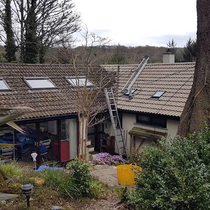 A roof being cleaned from a ladder in Marple, working off access equipment rather than walking on the tiles