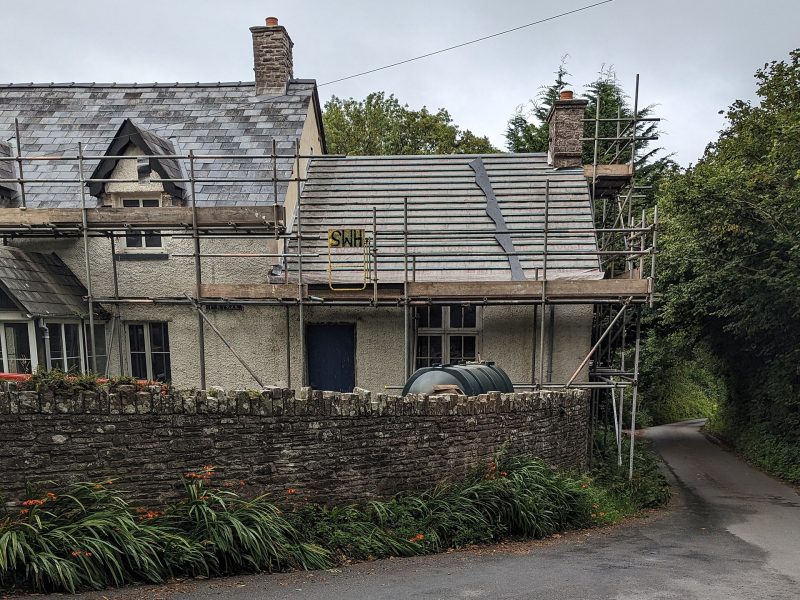 A stone cottage in Wales with scaffolding up for a re-roof, its slate roof stripped back to the battens