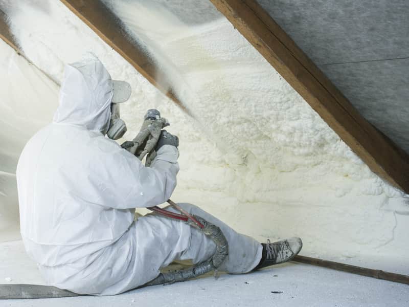 Closed cell spray foam being applied to the underside of a pitched loft roof, burying the rafters behind it