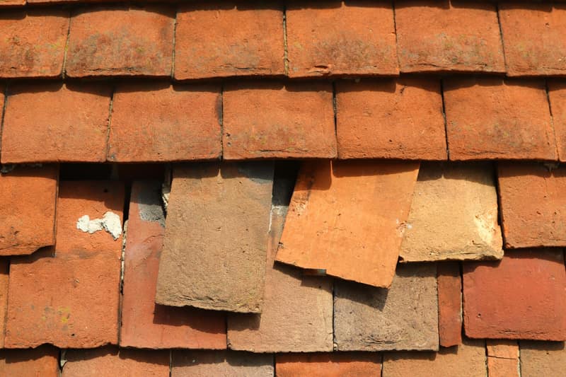 Slipped and missing plain clay tiles on a British roof after a storm, leaving the roof exposed underneath.